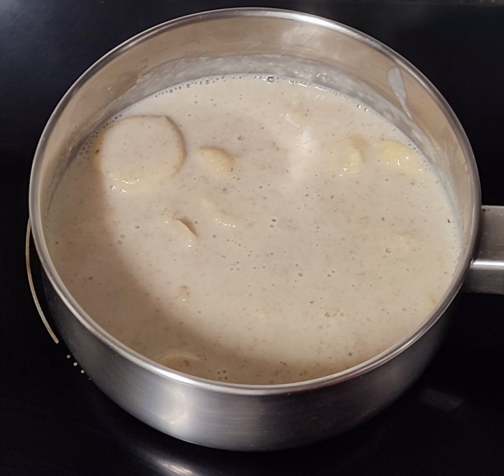 Olla vista desde arriba con leche, plátano y galletas calentándose en la vitrocerámica.