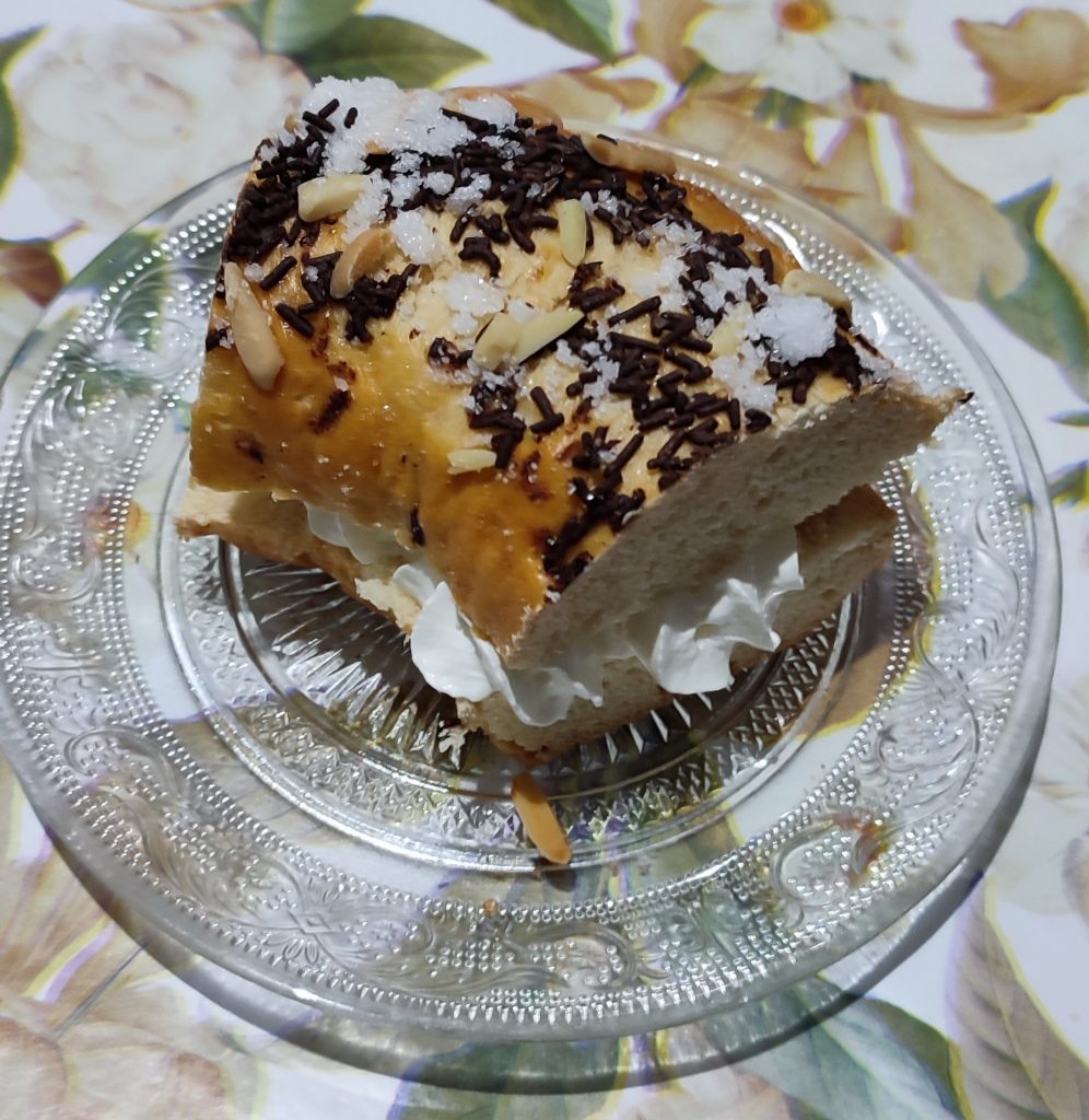 Porción de roscón relleno de nata servida en un plato de cristal sobre mantel floral.