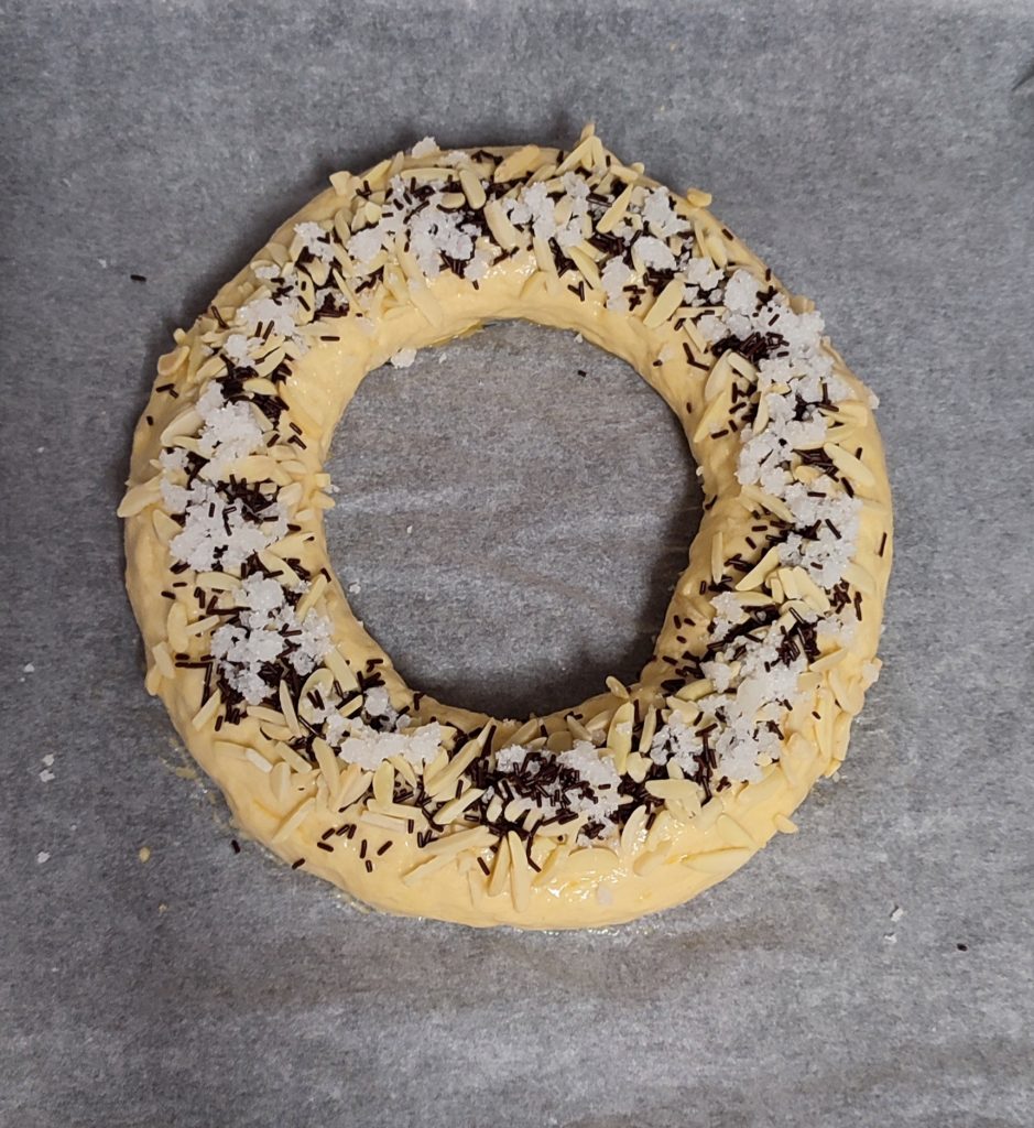 Roscón decorado con almendra laminada, fideos de chocolate y azúcar acristalado, colocado sobre papel de hornear.