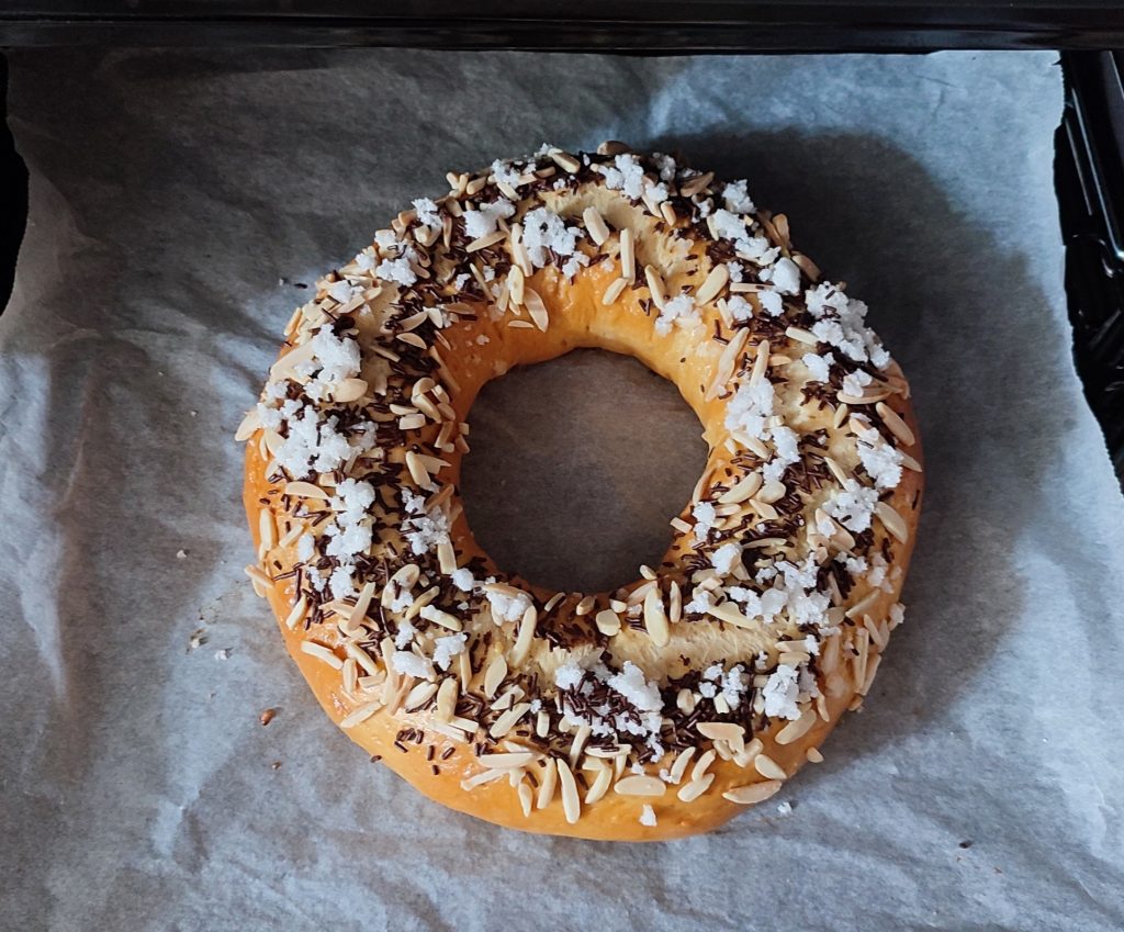 Roscón recién horneado sobre papel de horno, con la puerta del horno abierta y la bandeja parcialmente sacada.